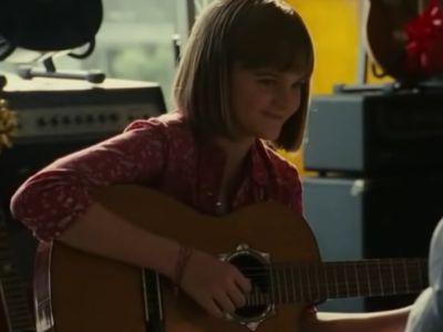 Casey Beane can be seen smiling as she is playing the guitar.